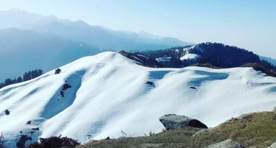 Mountain landscape with snow-covered peaks and clear blue sky.
