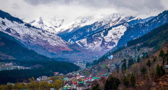 Manali's stunning mountains blanketed in snow, framed by vibrant green trees, showcase nature's beauty.