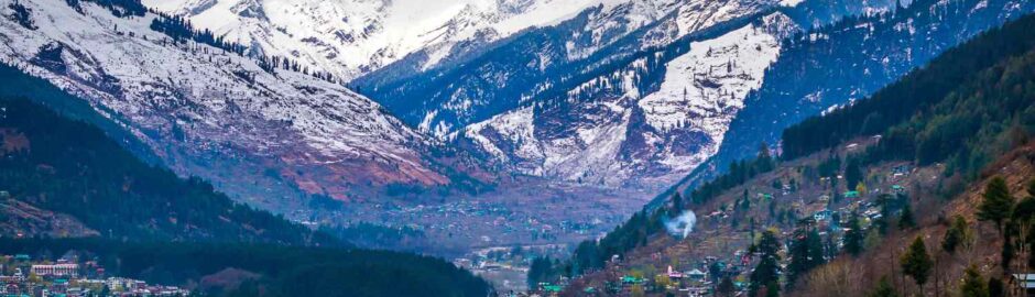 Manali's stunning mountains blanketed in snow, framed by vibrant green trees, showcase nature's beauty.
